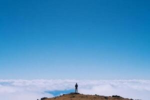 A person standing on top of a mountain with clouds in the background photo