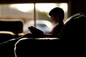 A boy sitting on a couch reading a book photo
