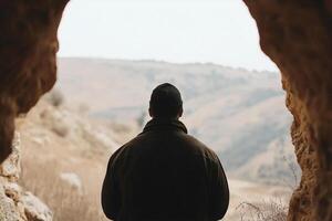 A man standing in a cave looking out over a valley photo