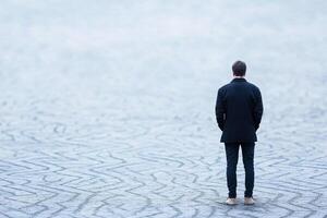 A man in a suit stands alone in the middle of a large field photo