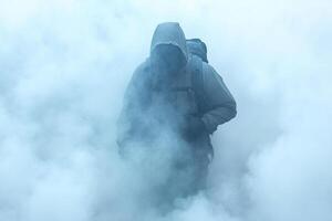 A man in a hoodie and backpack is standing in the fog photo
