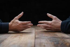 Two hands on a wooden table with one person making a gesture photo