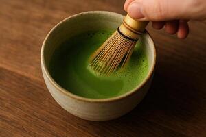 Preparation of Matcha Green Tea in Ceramic Bowl with Bamboo Whisk on Wooden Surface photo