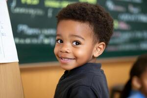 A young boy smiles at the camera while standing in front of a chalkboard photo