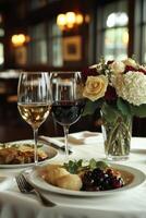 Two glasses of wine sit on a table next to delicious dishes, complemented by a lovely bouquet of flowers in a warmly lit restaurant during dinner service photo