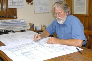 A man with a beard and glasses sitting at a desk with blueprints photo