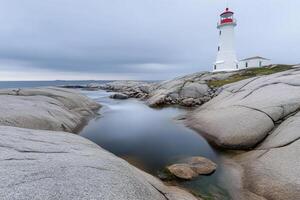 A lighthouse sits on the rocky shoreline of a body of water photo