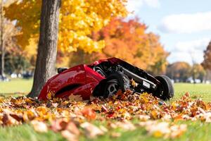 A red lawn mower laying on the ground in a park photo