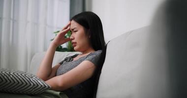 Handheld side view shot, Stressed young woman sits alone on a sofa, thinking aimlessly, feeling worried about something. Life problems video