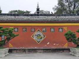 a chinese building with a large red wall and a tree in the middle photo