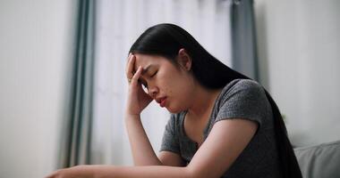 Handheld low angle view shot, Young Asian woman sit on the sofa alone, lost in thought. Her brows were slightly furrowed and expression tense in the quiet atmosphere at home video