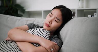 Handheld steady shot, A young woman is lying on a sofa, hugging a pillow, and thinking about something with stress and anxiety. video