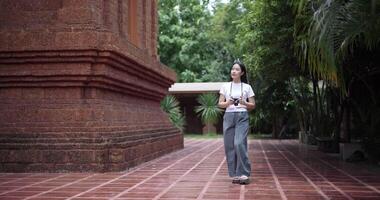 Handheld shot, Solo young female tourist enjoys taking photos with camera while taking a leisurely stroll amidst serene surroundings and the cultural richness of the place. video
