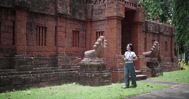 Handheld shot,Female tourist enjoys taking photos with camera while taking a leisurely stroll amidst serene surroundings and the cultural richness of the place. video