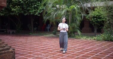 Handheld shot, Female tourist enjoys taking photos with camera while taking a leisurely stroll amidst serene surroundings and the cultural richness of the place. video