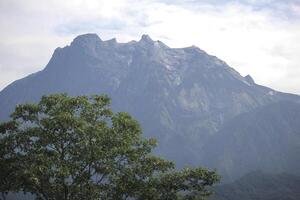 Majestic Mount Kinabalu Peak with Lush Greenery Under Cloudy Sky in Borneo photo