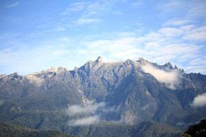 A breathtaking mountain peak with rugged rocky formations, partially covered by mist, under a cloudy sky photo