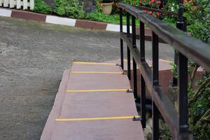 Concrete stairs with black metal handrails, highlighted with yellow safety lines, surrounded by lush greenery and colorful flowers in an outdoor setting photo
