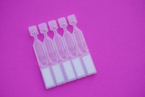 Single use artificial tear lubricant eye drops containers, tubes on pink background. Concept, medical products for dry eyes or eyes disease treatment. photo