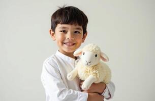 Happy child holding soft toy lamb against neutral background. Eid al-Adha photo