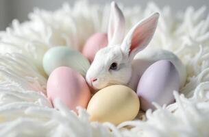 Adorable white bunny surrounded by pastel easter eggs on fluffy blanket photo