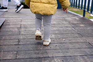 Child walks on wooden path near water in a bright yellow jacket during autumn photo