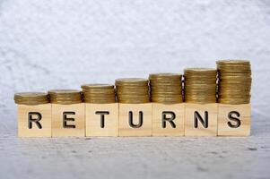 Returns text on wooden cubes with stacking golden coins. Business concept photo