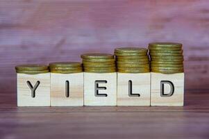 Yield text on wooden cubes with stacking golden coins. Business concept photo