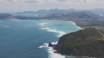 Waves crashing onto the shore of Lombok with lush hills in background video