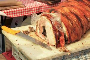 Close-up of Italian porchetta, a traditional pork roll, lying on a cutting board with a knife. photo