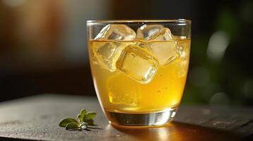 A refreshing glass of amber-colored liquid, with ice cubes, sits invitingly on a dark surface, casting a gentle glow. photo