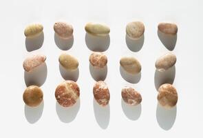 Aesthetic minimal pattern with set of sea pebble stones with sun shadow on light fon. Square composition from natural round smooth stone yellow beige color. Collection of rocks, top view photo