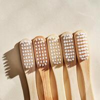 Eco friendly Bamboo toothbrushes with white bristles at sunlight with dark shadows on beige background. Sustainable living concepts, minimal style aesthetic photo, top view set wooden brushes photo