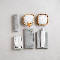 Natural spa, wellness, bath accessories as minimal flat lay pattern, sea salt flakes in wooden bowls, soft gray towels, brush, reusable cotton pads, grey concrete background, top view neutral photo