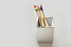 Ecofriendly Bamboo toothbrushes with colored bristles in square shaped grey concrete toothbrush holder at sunlight with shadows from window. Sustainable living concepts, minimal style aesthetic photo. photo