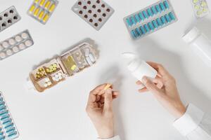 Pills box for daily intake of vitamins and medicines on white background. Top view glass of water and capsules and tablets in plastic container in woman hands. Lifestyle for beauty and health photo