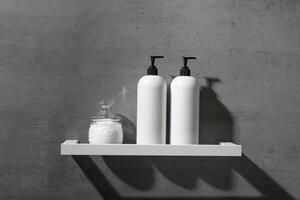 White bottles with shampoo, conditioner and bath salt on white shelf on gray concrete background. Aesthetic view beauty products in modern minimal bathroom neutral color. Side view, copy space photo