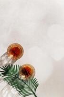 Whiskey Glasses with Shadows and sunlight Reflection on beige background, glass strong alcohol, palm leaf decor, aesthetic top view summer still life, refraction at crystal shine cups, caustics photo