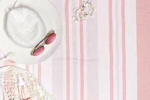 Summer flat lay with sun hat, sunglasses, cosmetics products on striped beach towel as background. Summer holiday, vacation, rest concept. Top view summertime accessories, white pink pastel color fon. photo