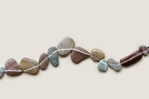 Creative arrangement of natural colored stones. Smooth pebbles in row on beige background. Minimal trend summer flat lay, top view still life composition with sea pebble on the same line photo