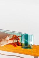 Vibrant still-life with colorful transparent glass mug or cup in shades of green teal and orange. Sunlight dynamic shadows and reflections on white, minimal aesthetic design, table setting photo
