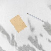 Pencil and craft blank paper card on grey marble background, copyspace. Minimalist summer lifestyle concept in natural daylight with plant shadows on table, holiday happy wishes template, top view photo