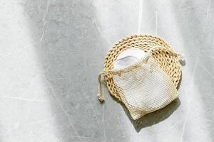Beige mesh bag with reusable cotton pads decorated dried flower on marble table background, natural light and shadows. Eco-friendly and sustainable beauty routine, self-care and zero-waste concept photo