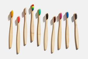 Eco friendly Bamboo toothbrushes with colored bristles at sunlight with dark shadows on white background. Sustainable living concepts, minimal style aesthetic photo, top view set wood oral brushes photo