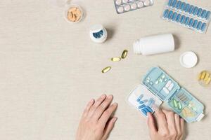 Top view women hands with medical tablets, capsules, nutrition supplements on tablecloth. Medicine pill box, weekly pill organizer with vitamins, minerals. Flat lay medical background photo