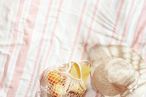 Summer Lifestyle flat lay with sun hat, fresh citrus fruits, oranges, book for read on striped beach towel, pastel pink background, palm shadow. Summer beach day, relaxation, rest time photo
