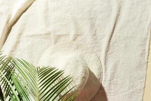 Summer minimal background, top view wide brimmed sun hat under palm leaf on beach towel on sand. Summer aesthetic photography pastel beige colored, copy space, vacation, relaxation concept. photo