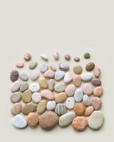 Creative arrangement of natural colored sea stones. Smooth round pebbles as square pattern on beige background. Minimal trend summer flat lay, top view still life composition with rocks photo