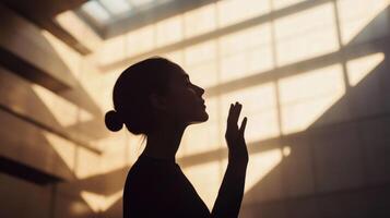 A midaged figure silhouetted against a softly blurred backdrop of angular modern structures raises an open palm to their face signifying deep reflectio photo