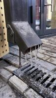 Icy scene of frozen icicles hanging from drainpipe. The image captures cold weather effects and seasonal change on metal pipe, with ice forming near ground photo